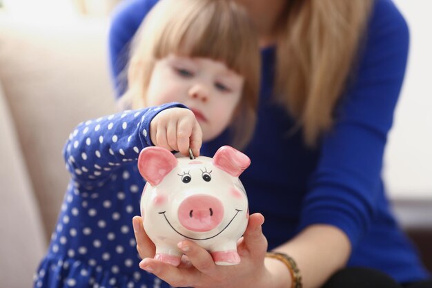 A little girl puts a coin in a pink piggy bank