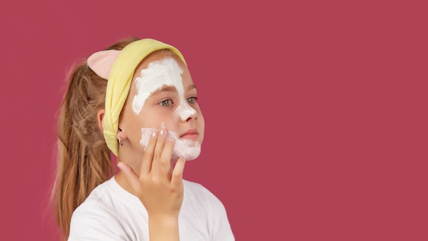 A little girl puts on a cosmetic mask on an isolated red.