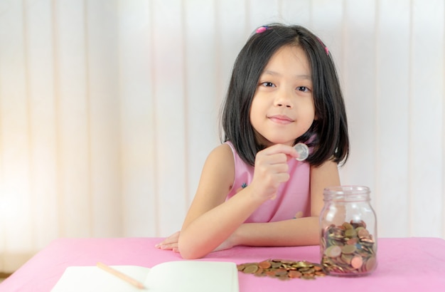 小さな女の子が貯金箱にコインを入れて、子供のお金の概念を保存します。