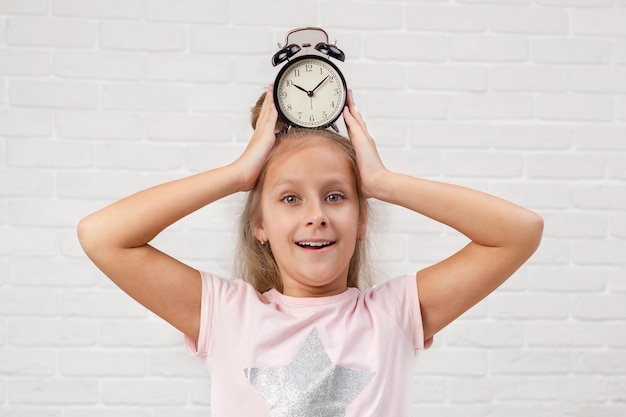 Photo little girl in pyjamas with clock