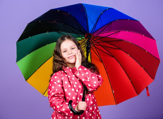 レインコートを着た少女カラフルな傘の雨よけを持った幸せな少女レインボー秋のファッション前向きな気分で陽気なヒップスターの子供彼女の自由を楽しんでいます