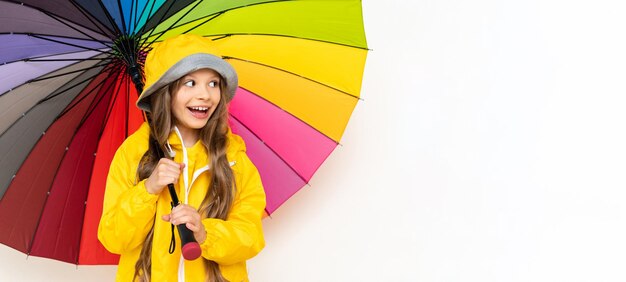 A little girl in a raincoat holds a multicolored umbrella on a white isolated background Rainy weather copy space