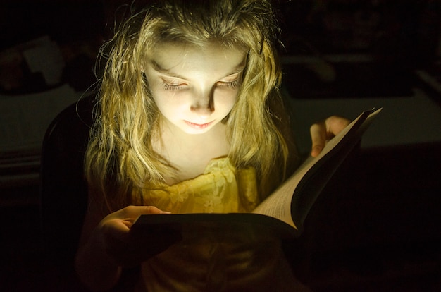 Little girl read a book in dark room. 