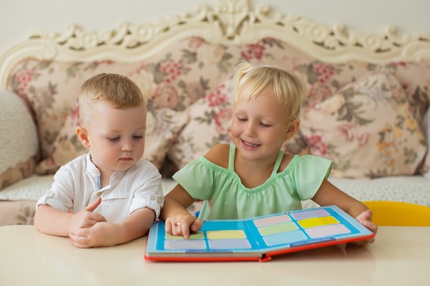 Маленькая девочка читает книгу для брата дома