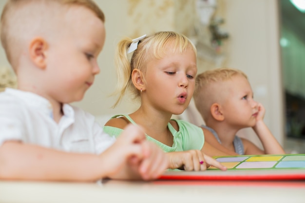 Little Girl Reading Book to Brothers at Home