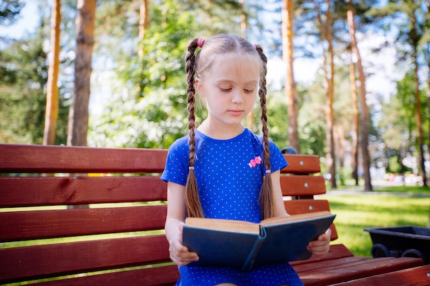 Маленькая девочка читает книгу на открытом воздухе.