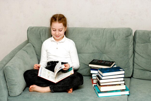 Photo little girl reading a book sitting on the sofa