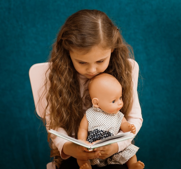 Little girl reads a book to a doll