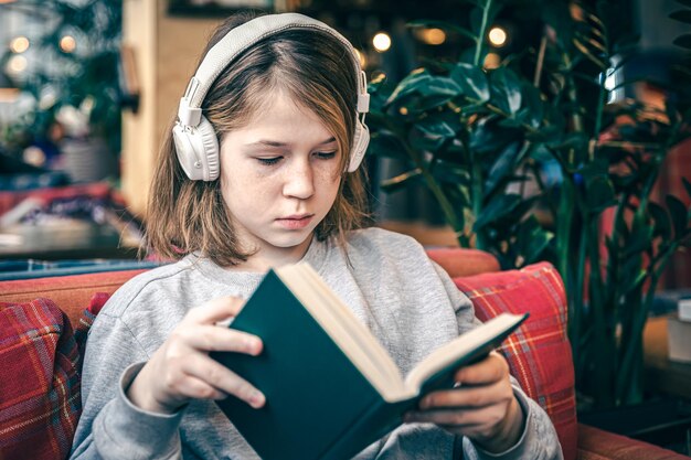 A little girl reads a book and listens to music on headphones