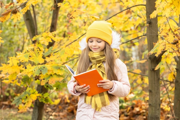 A little girl reads a book in the woods in autumn.