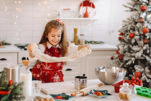 新年のキッチンで赤いエプロンを着た少女がクリスマスクッキーの生地を準備します