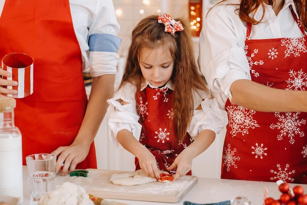 A little girl in a red apron in the New Year's kitchen prepares dough for Christmas cookies