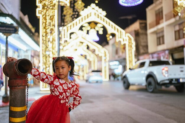 Little girl in red dress standing in city against decorated light tunnel background