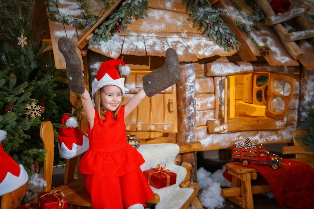 クリスマスプレゼントと素晴らしい家の近くのフェルトブーツと赤いドレスを着た少女