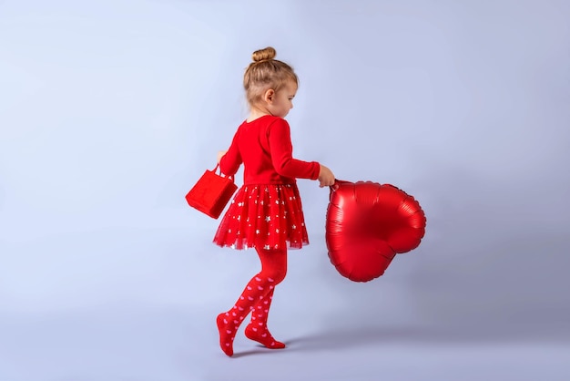 маленькая девочка в красном платье с воздушным шаром в форме сердца в руках