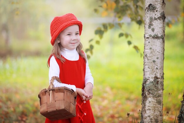 A little girl in a red hat and dresses is walking in the park. Cosplay for the fairytale hero "Little Red Riding Hood"