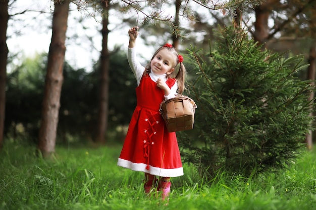 A little girl in a red hat and dresses is walking in the park. Cosplay for the fairytale hero "Little Red Riding Hood"