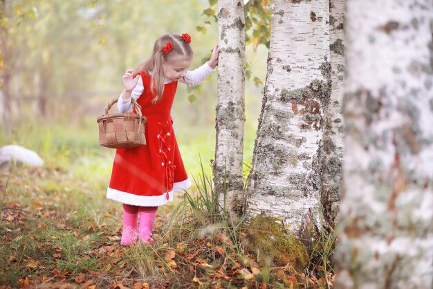 A little girl in a red hat and dresses is walking in the park. Cosplay for the fairytale hero "Little Red Riding Hood"