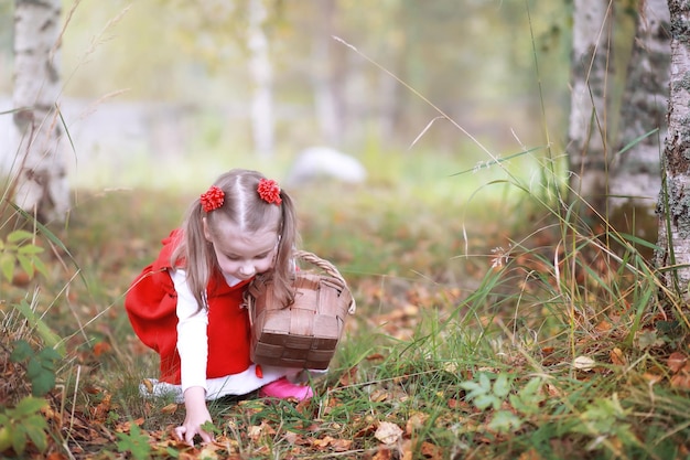 赤い帽子とドレスを着た少女が公園を歩いています。おとぎ話の主人公「赤ずきん」のコスプレ