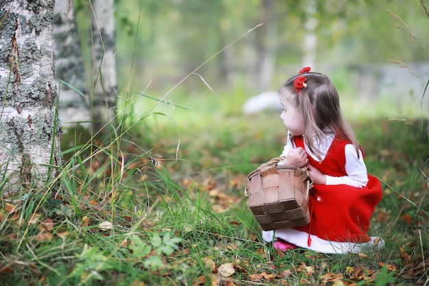 赤い帽子とドレスを着た少女が公園を歩いているおとぎ話のヒーロー赤ずきんのコスプレ