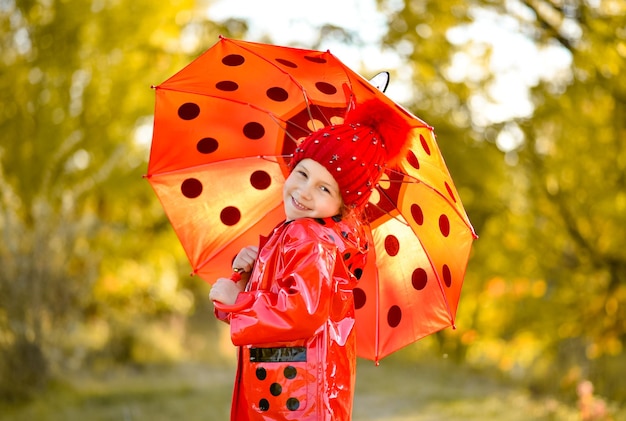 A little girl in a red hat  a red polka dot jacket with a red umbrella in nature Autumn Atmosphere