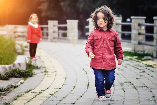 Photo a little girl in a red jacket walks down a path with a girl in the background.