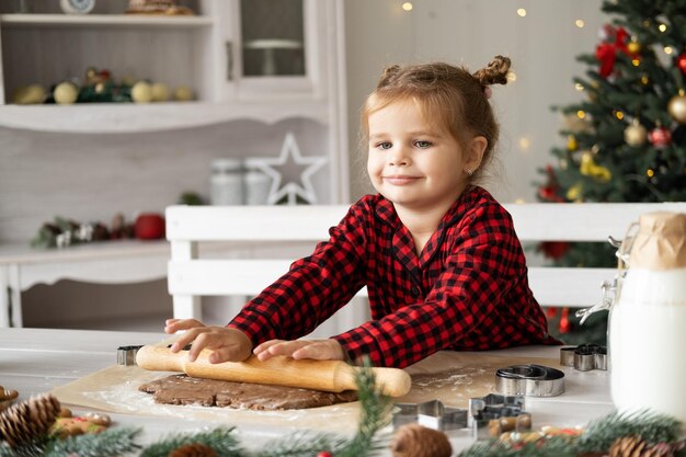 Little girl in red pajama cooking festive gingerbread in christmas decorated kitchen