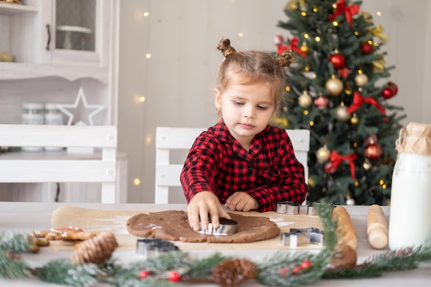 クリスマスに飾られたキッチンでお祝いのジンジャーブレッドを調理する赤いパジャマの少女