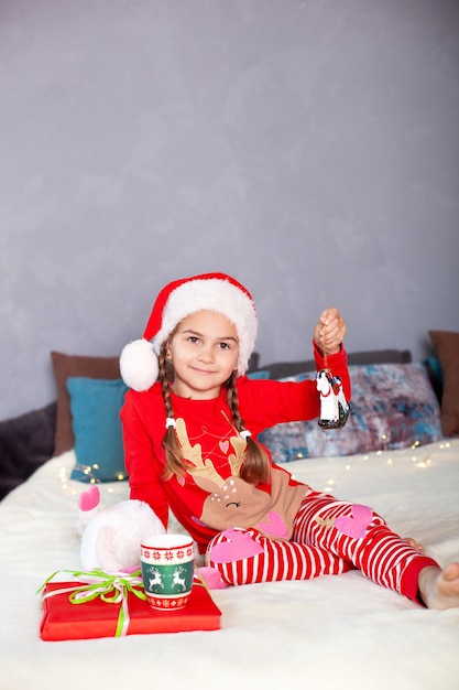 Little girl in red pajamas and Santa Claus hat on bed