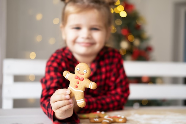 장식된 크리스마스 진저 브레드 남자 쿠키를 들고 빨간 잠옷을 입은 어린 소녀