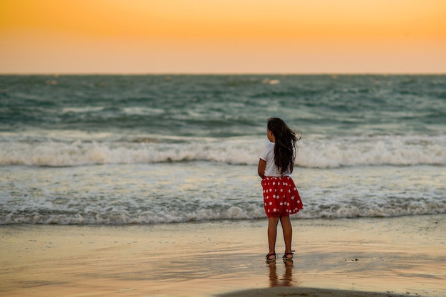 Little girl in a red skirt in white peas runs along the seashore