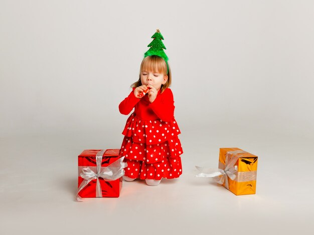 Little girl in red suit opens gift box isolated on yellow background