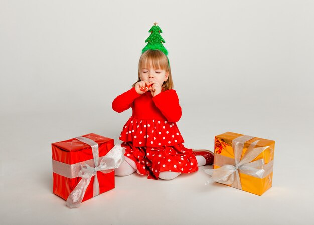 Little girl in red suit opens gift box isolated on yellow background