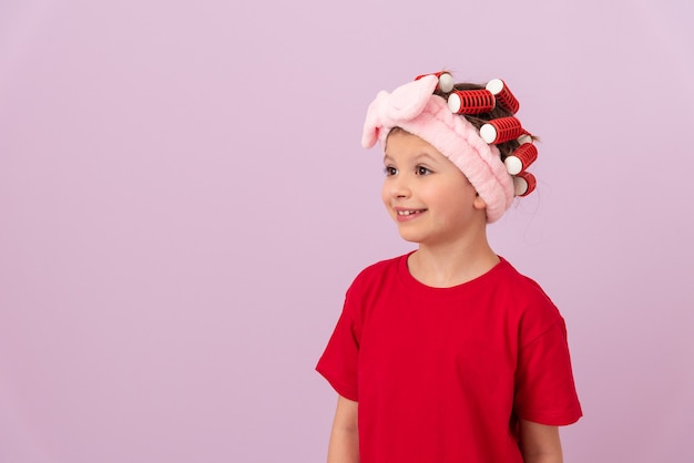 A little girl in a red T-shirt with curlers on her head is smiling.