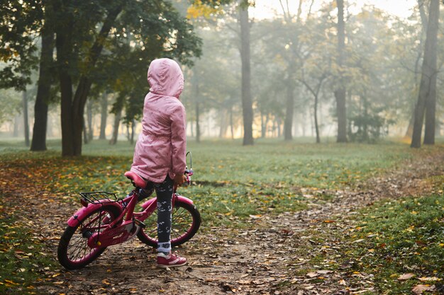 日の出の美しい秋の霧の日に彼女の自転車に乗る少女