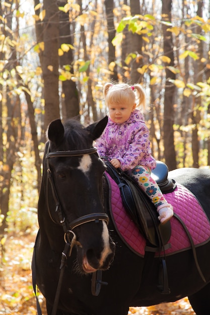 Little girl riding a horse in the autumn forest