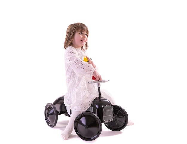 Photo little girl riding retro style toy car. girl riding old metal pedal car for children