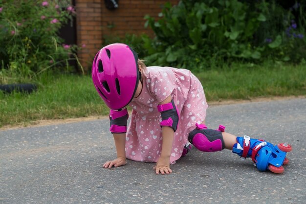 完全に保護された小さな女の子のローラースケートがアスファルトに落ちました。安全な乗り心地のコンセプト。