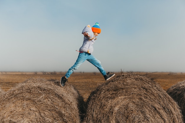 Little girl run and jump on haystacks on the farm.