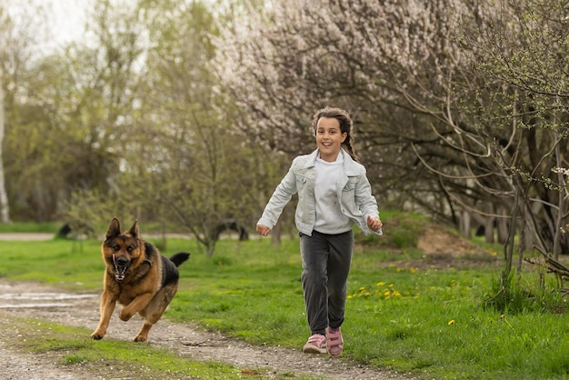 Маленькая девочка бежит с собакой в цветочном саду