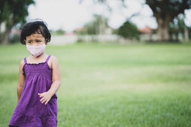 들판을 걷고 있는 보호용 안면 마스크를 쓴 어린 소녀 슬픈 얼굴 표정