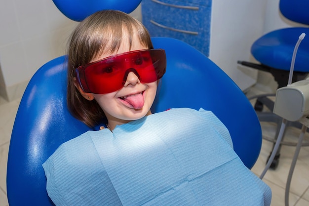 A little girl in the safety glasses at the dentists is showing her tongue