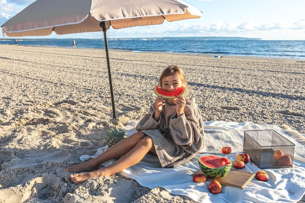 A little girl on a sandy sea beach eats a watermelon