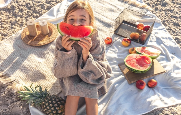 A little girl on a sandy sea beach eats a watermelon