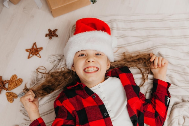 Little girl in a santa claus hat lies near the christmas tree at home. view from above. Christmas.