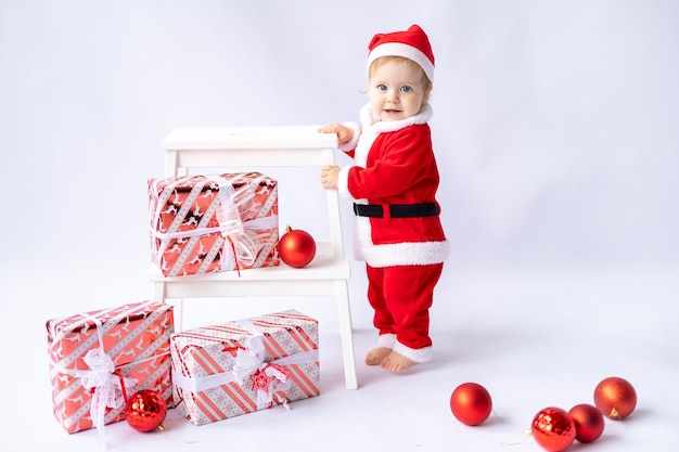 A little girl in a Santa costume stands with Christmas gifts in boxes on a white background newyea