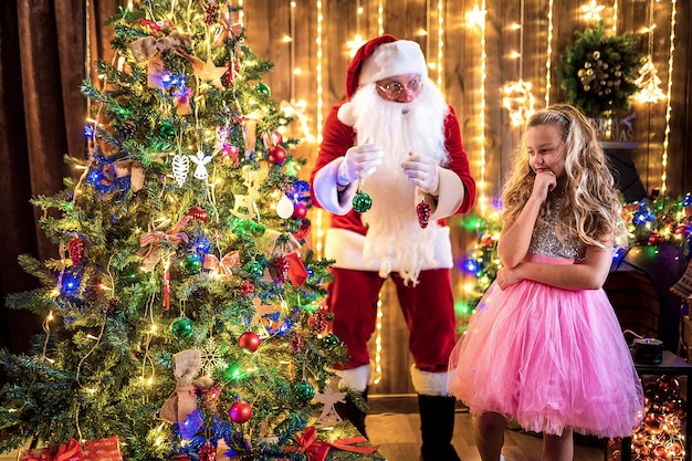 小さな女の子とサンタがクリスマスツリーを飾る