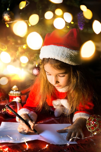 크리스마스 트리 아래 산타 모자에있는 어린 소녀가 꿈을 꾸고있다