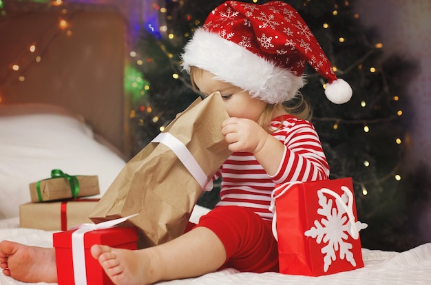 Little girl in Santa hat opening Christmas gift box Funny and expressive toddler enjoying gifts