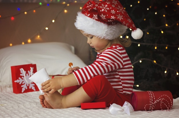 Little girl in Santa hat opening Christmas gift box Funny and expressive toddler enjoying gifts